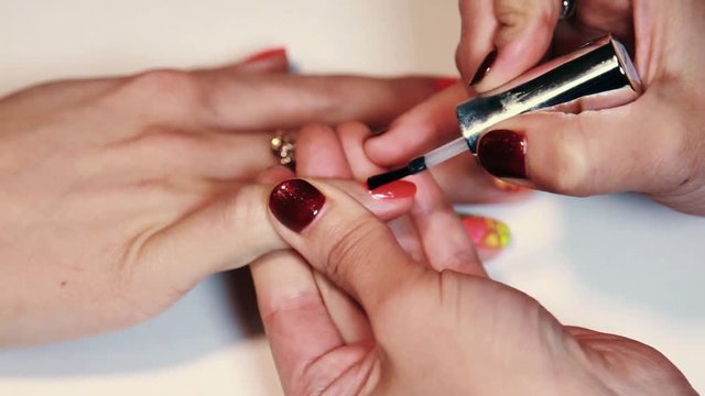 Woman hands glossing transparent polish on finger nails over white surface, close up