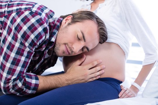 Man listening to pregnant womans belly in ward