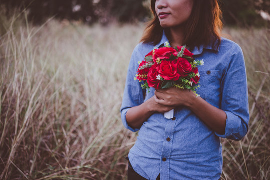 Young hipster woman in field holding a bouquet of red rose.