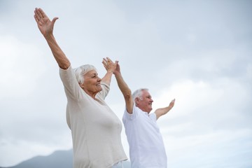 Senior couple standing with arms outstretched on the beach
