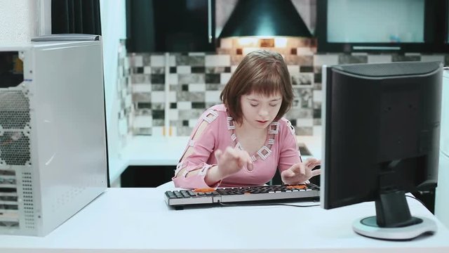 Girl with Down syndrome sitting at a computer at home and typing text. . March 21, 2017 World Down Syndrome Day.