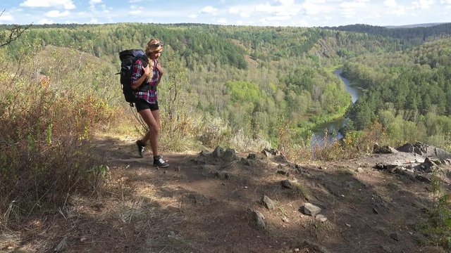 Young blonde woman tourist with a backpack goes on mountain trail. Russia, Siberia, Salair