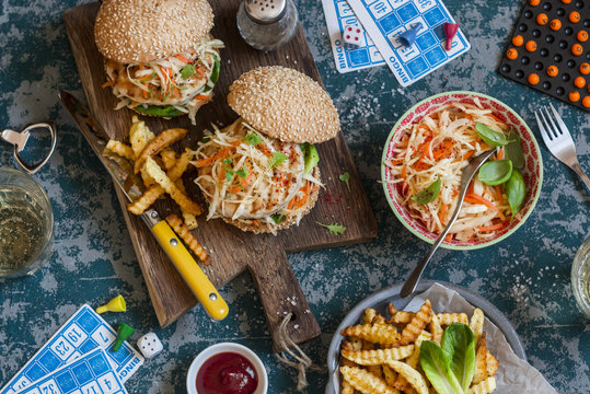 Hamburgers with grilled chicken and cole slaw on a wooden board on the table with cards and bingo chips, top view. Flat lay