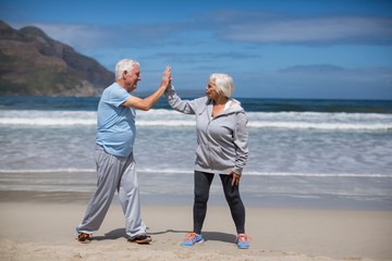 Senior couple giving high five after exercise on the beach