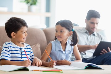 Smiling siblings doing homework in living room
