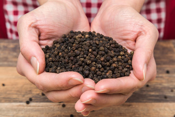 Black pepper grain in the hands on the table in the kitchen. Healthy eating and lifestyle.