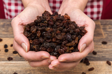 Raisins in the hands on the wooden table in the kitchen. Healthy eating and lifestyle.