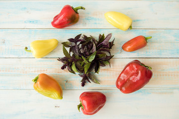 Pepper. Red, orange, yellow around a bunch of Basil on wooden table