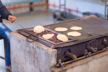 Man cooking Indian flat bread, called chapati, and roasting it on live flame.