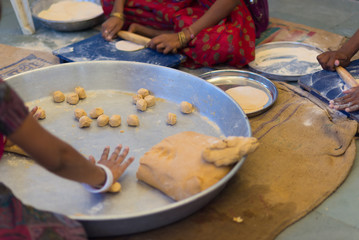 Women making Indian flat bread, called chapati, on a big silver plate.