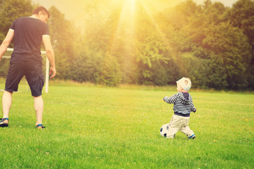 Little boy playing football on the field with gates