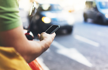 Man pointing on screen smartphone on background cars, tourist hipster using in hands mobile phone, traveler connect wifi internet and calls taxi, headlights auto on backdrop city street, mockup