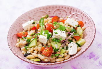 Salad of white beans, tomato, celery, cucumber, arugula, red onion and feta cheese in bowl. Diet...