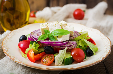 Greek salad with fresh tomato, cucumber, red onion, basil, lettuce, feta cheese, black olives and a Italian herbs on plate.