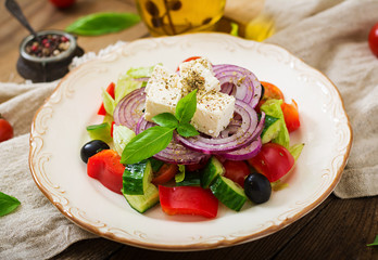 Greek salad with fresh tomato, cucumber, red onion, basil, lettuce, feta cheese, black olives and a Italian herbs on plate.