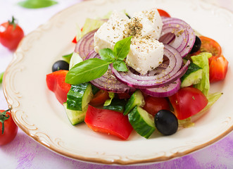Greek salad with fresh tomato, cucumber, red onion, basil, lettuce, feta cheese, black olives and a Italian herbs on plate.