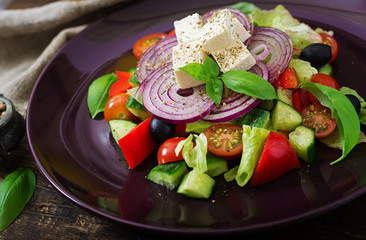 Greek salad with fresh tomato, cucumber, red onion, basil, lettuce, feta cheese, black olives and a Italian herbs on plate.