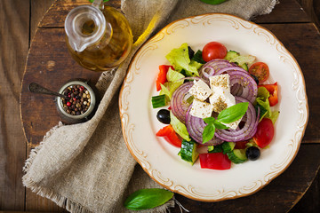 Greek salad with fresh tomato, cucumber, red onion, basil, lettuce, feta cheese, black olives and a Italian herbs on plate. Flat lay. Top view