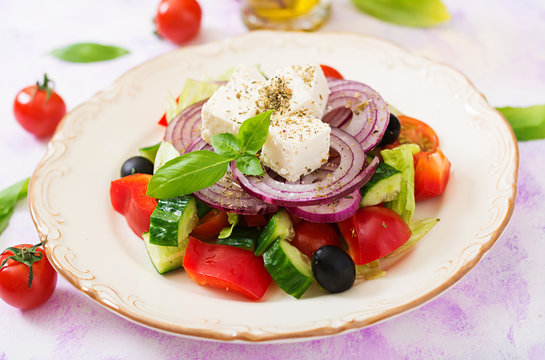 Greek salad with fresh tomato, cucumber, red onion, basil, lettuce, feta cheese, black olives and a Italian herbs on plate.