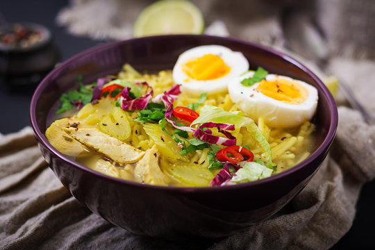 Noodle soup with chicken, celery and egg in a bowl on a old wooden background.