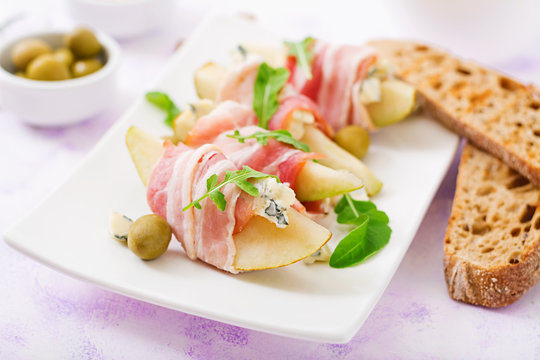 Appetizer with pear, blue cheese, prosciutto ham and toast for holidays on a white plate.