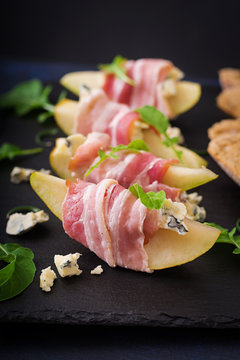 Appetizer with pear, blue cheese, prosciutto ham and toast for holidays on a dark plate.