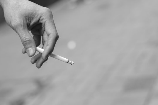 man hand holding smoking a cigarette with smoke cigarette in black and white / monotone image