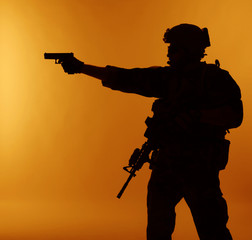 Fototapeta na wymiar United states Marine Corps special operations command Marsoc raider with weapon aiming pistol. Silhouette of Marine Special Operator orange background
