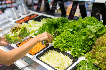 Women buying salad bar with vegetables in supermarket
