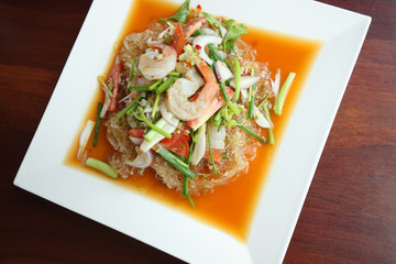 Thai spicy seafood salad on white dish, top view.