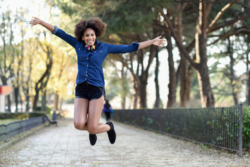 Fototapeta na wymiar Young black woman with afro hairstyle jumping in urban backgroun