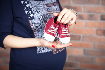 belly of a pregnant woman in a blue dress, mother hands holding shoes for the newborn girl