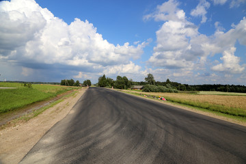 Fototapeta na wymiar Landstraße mit Reifenspuren unter weitem blauem Himmel in Lettland