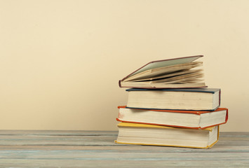 Book stacking. Open hardback books on wooden table and beige background. Back to school. Copy space for ad text.