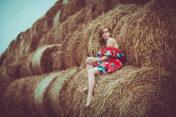 Happy woman on hay stack in sunny day. Beauty romantic girl outdoors against  . Photo of sexy brunette in a field with haystacks