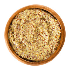 Whole grain Dijon mustard in wooden bowl with brown seeds. Traditional mustard named after the town of Dijon in Burgundy, France. Isolated macro food photo close up from above on white background.