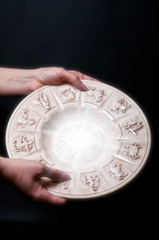 a woman keeping astrology plate with zodiac signs with copy space over a black background 