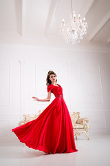 Elegant woman in a long red dress is standing in a white room, dress swirl