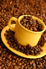 Yellow coffee cup with beans over brown background with seeds and copy space 