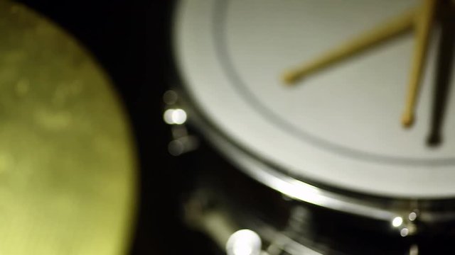 Dolly shot of a cymbal, a snare drum and a pair of drumsticks, with focus transition.