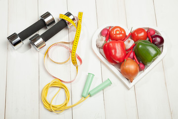 Sport and diet. Healthy lifestyle. Vegetables, dumbbells. Peppers, tomatoes, garlic, onion radish in a heart on white background