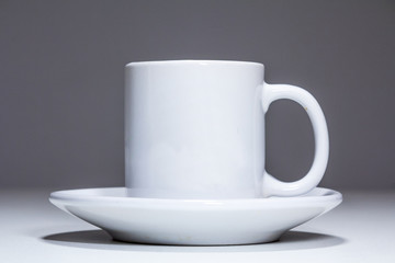 White coffee cup on a grey background..Picture of a white coffee cuf lit with a grey bacground made of shadows