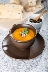Brown cup with squash soup, roll with olives