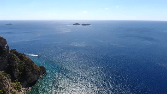 Aerial flying over sea near rocky cliff coastline left beautiful coastal landscape with ocean in background and speedboat moving over blue tropical sea amazing place for tourism visit vacation 4k