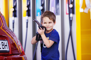 small boy holds a fuel nozzle near the red car