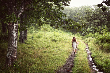 Young girl from the back in a dress walking alone on in a forest 