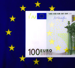 One hundred euro bill lying in the center of the star circle on the European community flag. Square macro image.
