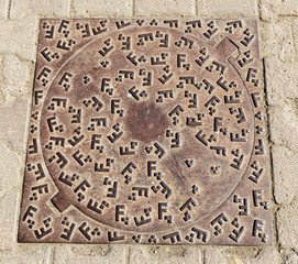 In the picture we can see a circular design of a classic art on a manhole cover.