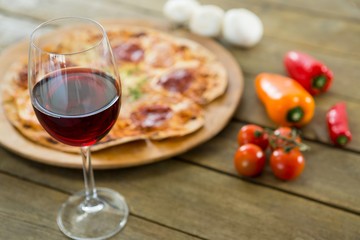 A glass of red wine served with italian pizza in the background