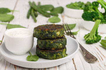 Green pancakes with broccoli, zucchini, green beans, asparagus and spinach with the yogurt sauce and ingredients on a white table. Vegetable fritters. Healthy Breakfast. Selective focus
